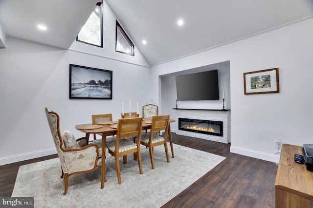 dining space featuring baseboards, dark wood-style floors, high vaulted ceiling, a glass covered fireplace, and recessed lighting