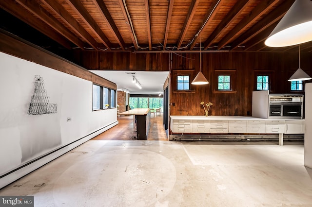misc room featuring a baseboard heating unit, concrete flooring, wood walls, and plenty of natural light