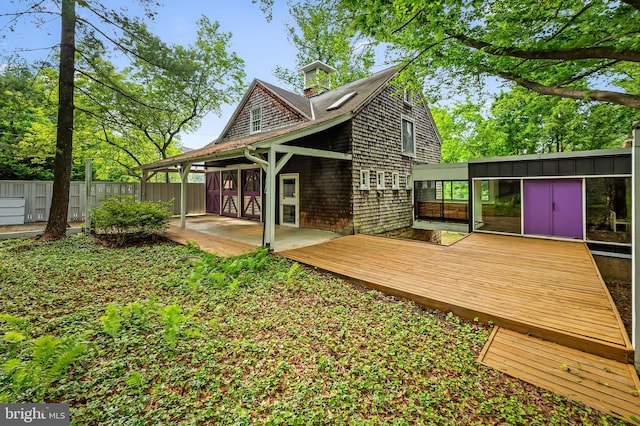 back of house with a wooden deck, a chimney, and a patio