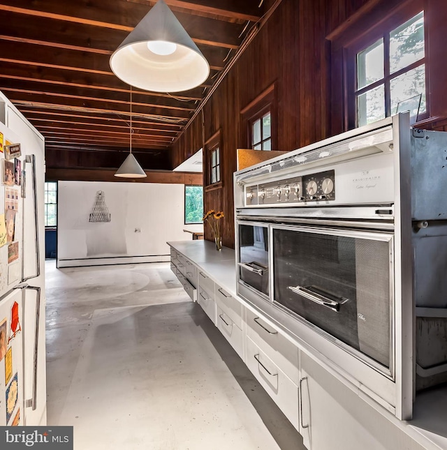 kitchen with concrete floors, freestanding refrigerator, stainless steel oven, white cabinetry, and healthy amount of natural light