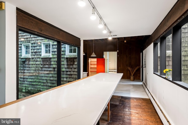 corridor with a baseboard heating unit, wood finished floors, and track lighting