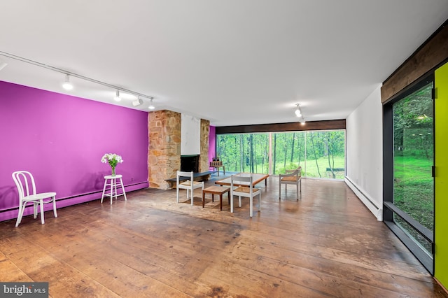 dining room featuring baseboard heating, wood-type flooring, track lighting, and a stone fireplace