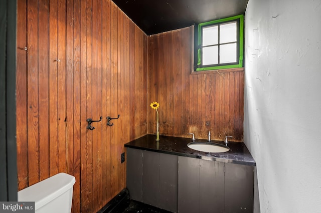 half bathroom with a sink, wood walls, and toilet