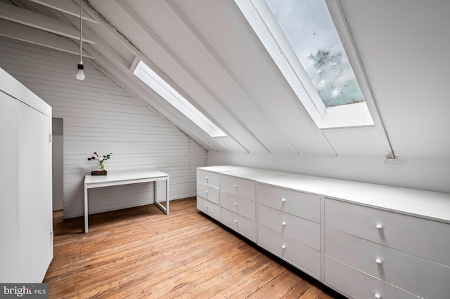additional living space with a skylight, lofted ceiling, light wood-style floors, and wooden walls