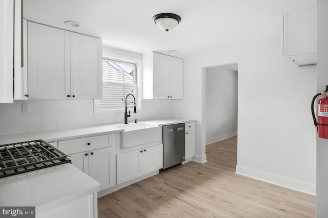 kitchen with stainless steel dishwasher, baseboards, a sink, decorative backsplash, and light wood-type flooring