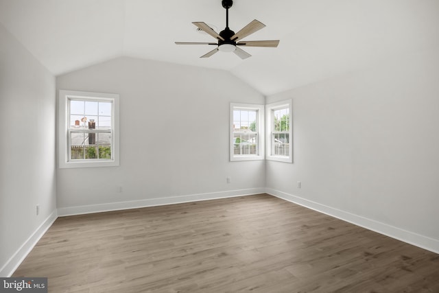 empty room featuring healthy amount of natural light, ceiling fan, wood finished floors, vaulted ceiling, and baseboards