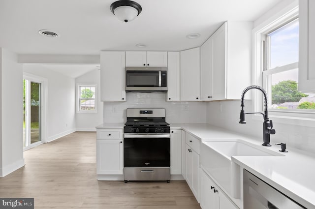 kitchen with appliances with stainless steel finishes, a sink, white cabinets, light countertops, and backsplash