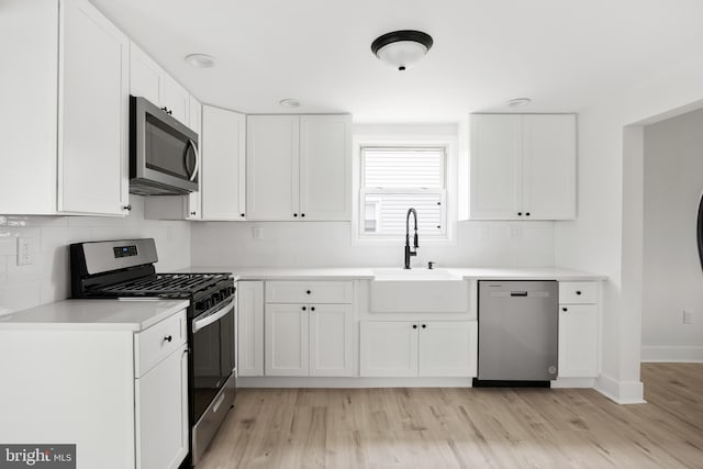 kitchen with appliances with stainless steel finishes, a sink, light wood-style flooring, decorative backsplash, and white cabinetry