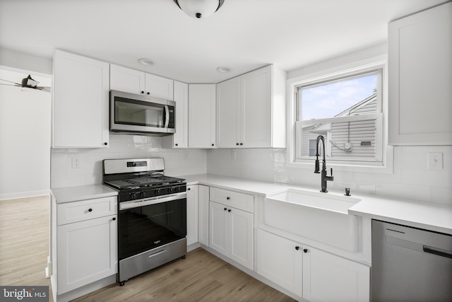 kitchen featuring stainless steel appliances, a sink, decorative backsplash, white cabinetry, and light countertops