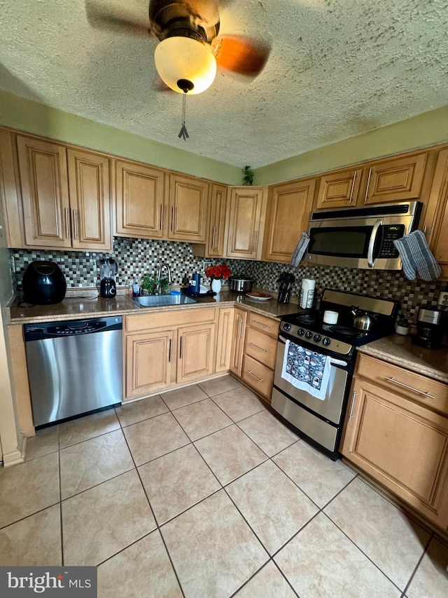 kitchen with stainless steel appliances, decorative backsplash, a sink, light tile patterned floors, and a textured ceiling
