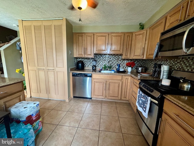 kitchen featuring appliances with stainless steel finishes, a sink, tasteful backsplash, a textured ceiling, and light tile patterned floors