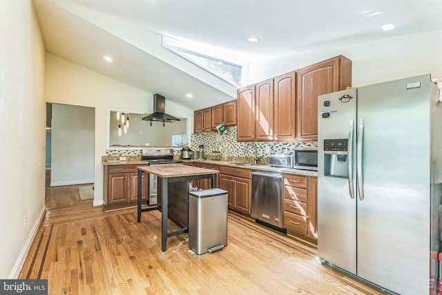 kitchen featuring stainless steel appliances, wall chimney exhaust hood, backsplash, a sink, and light wood-type flooring