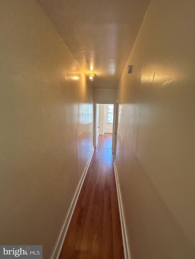 corridor with dark wood-style flooring and baseboards