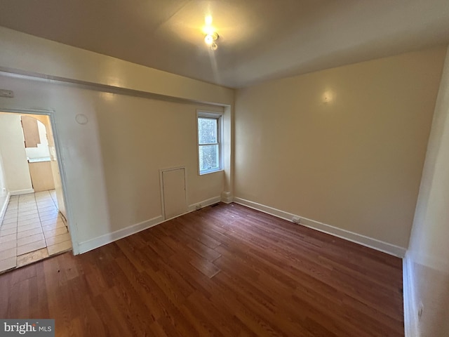 empty room featuring wood finished floors, baseboards, and arched walkways