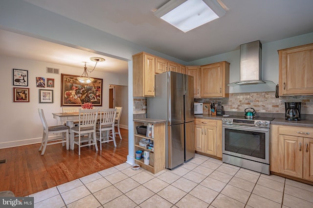 kitchen with appliances with stainless steel finishes, wall chimney exhaust hood, light brown cabinets, tasteful backsplash, and light tile patterned floors