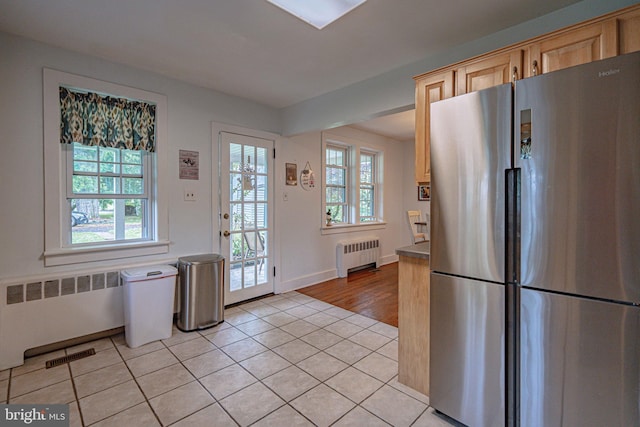 kitchen with freestanding refrigerator, radiator, plenty of natural light, and light tile patterned floors