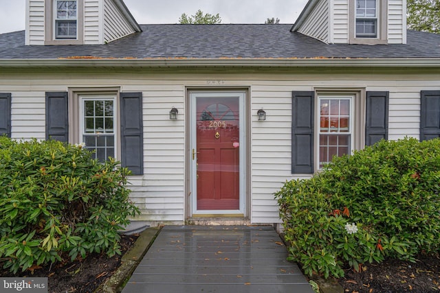 doorway to property with roof with shingles and a deck
