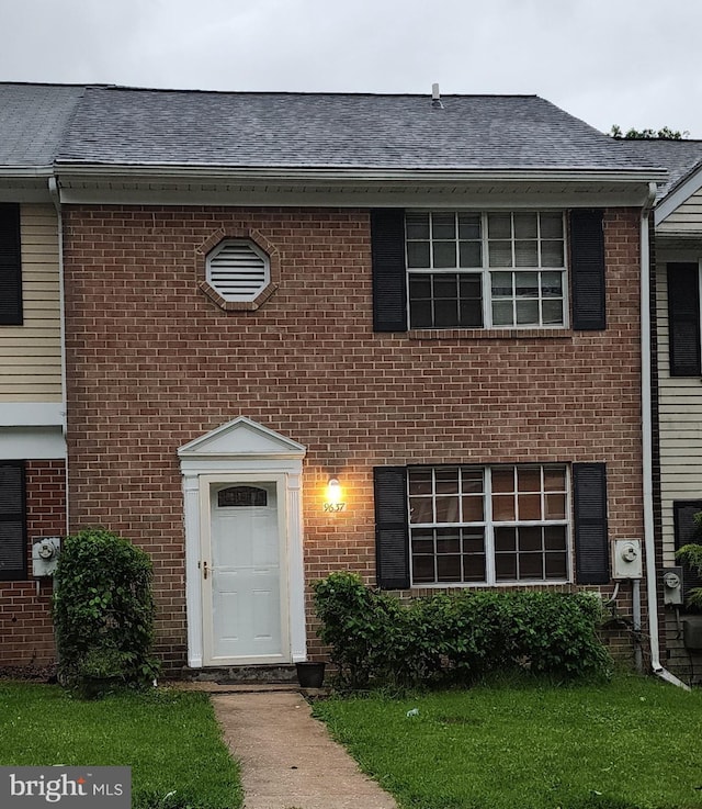 view of property featuring brick siding and roof with shingles