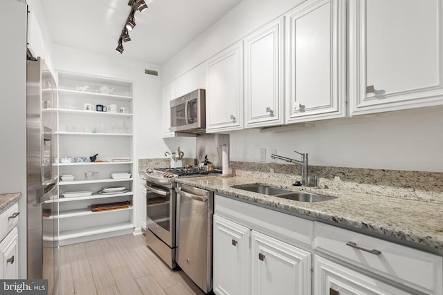 kitchen with a sink, appliances with stainless steel finishes, white cabinets, light stone counters, and open shelves