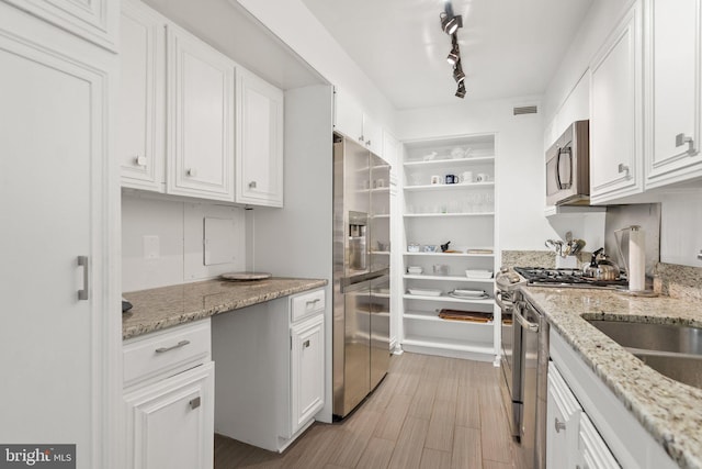 kitchen with appliances with stainless steel finishes, white cabinets, light wood-style floors, and light stone counters