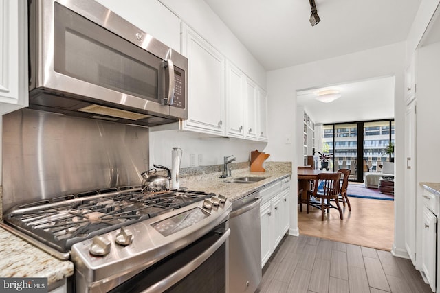 kitchen featuring appliances with stainless steel finishes, a sink, white cabinetry, and light stone countertops