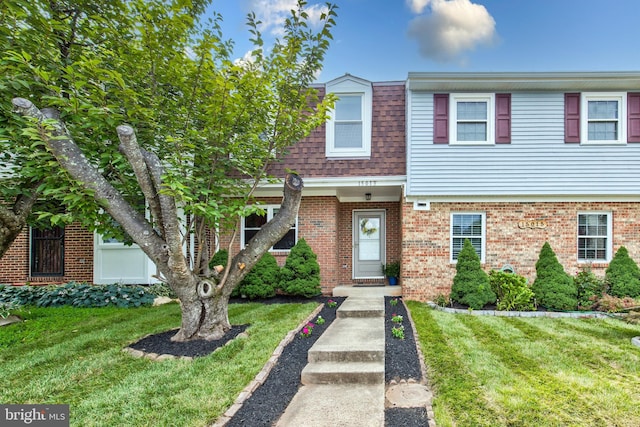 townhome / multi-family property with a front lawn, brick siding, and a shingled roof