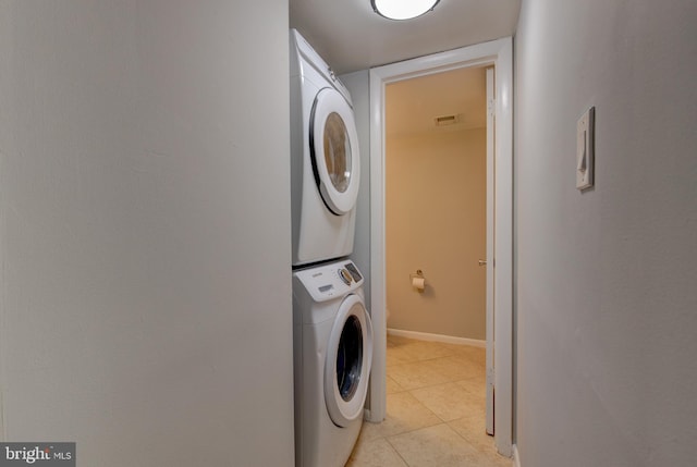 clothes washing area with stacked washer / dryer, light tile patterned floors, and baseboards