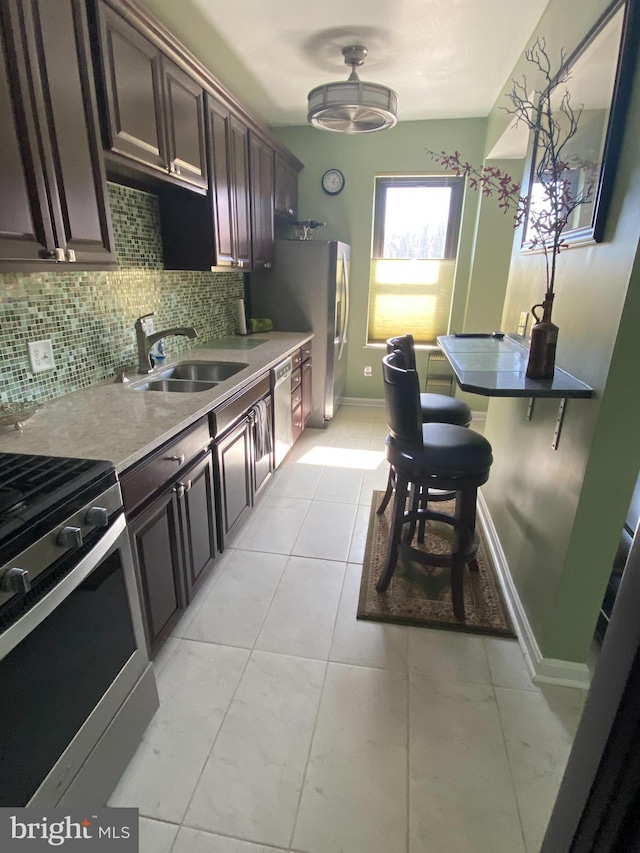 kitchen with a sink, appliances with stainless steel finishes, backsplash, dark brown cabinets, and baseboards