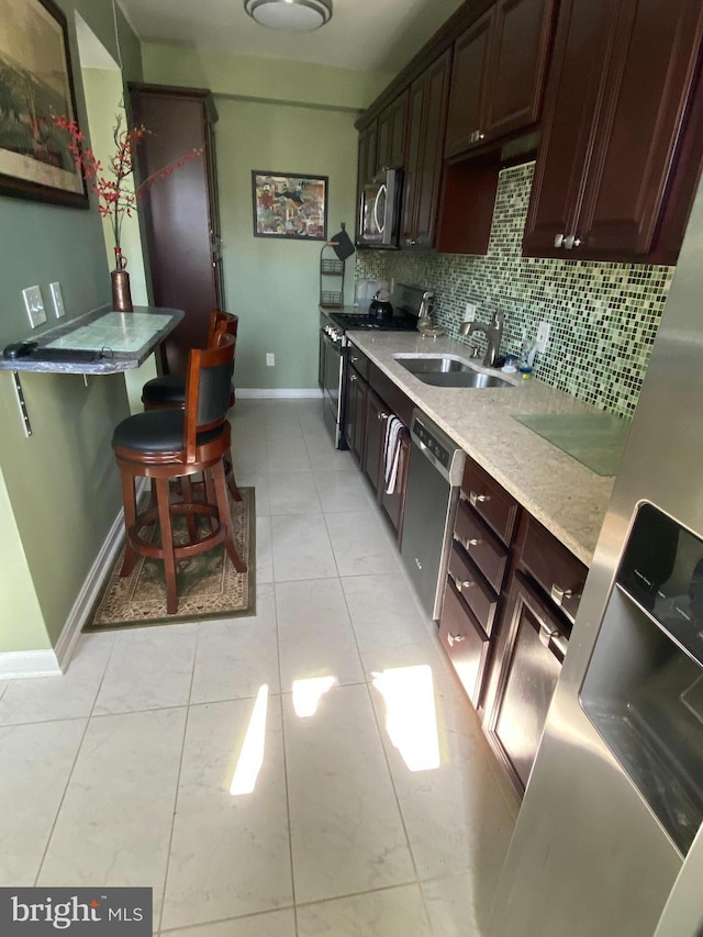 kitchen with appliances with stainless steel finishes, a sink, baseboards, backsplash, and dark brown cabinets