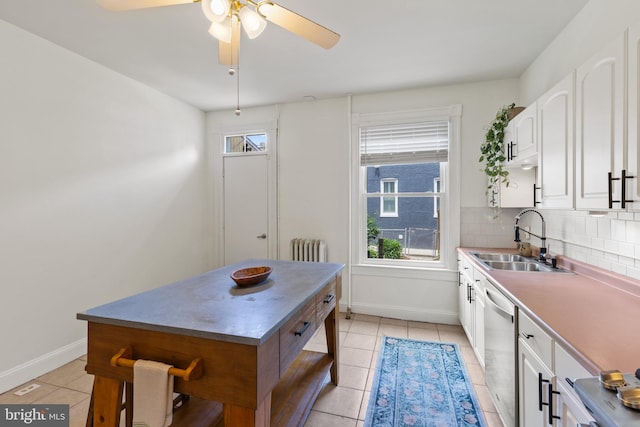 kitchen with a sink, radiator, stainless steel dishwasher, light tile patterned floors, and white cabinetry