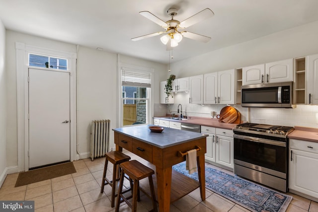kitchen featuring stainless steel appliances, open shelves, radiator, decorative backsplash, and white cabinets