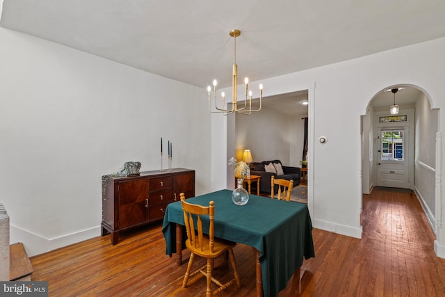 dining room featuring arched walkways, a chandelier, wood-type flooring, and baseboards