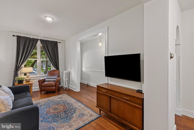 living room with radiator, wood finished floors, arched walkways, and baseboards