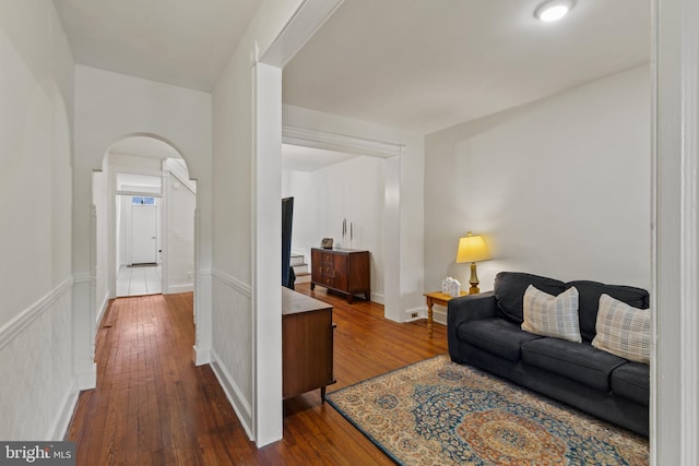 living area featuring arched walkways, dark wood-style floors, and a wainscoted wall