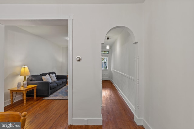 corridor with hardwood / wood-style flooring, arched walkways, and baseboards