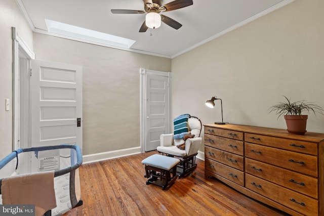 sitting room with a ceiling fan, wood finished floors, crown molding, a skylight, and baseboards