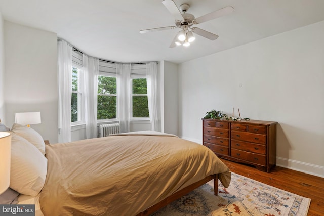 bedroom featuring radiator heating unit, baseboards, wood finished floors, and a ceiling fan