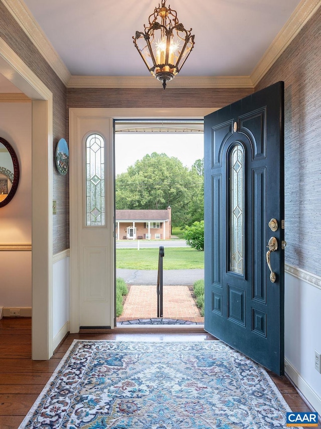 foyer entrance featuring baseboards, wallpapered walls, ornamental molding, wood finished floors, and a chandelier