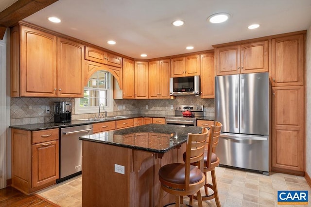 kitchen featuring appliances with stainless steel finishes, a sink, a breakfast bar area, dark stone counters, and recessed lighting