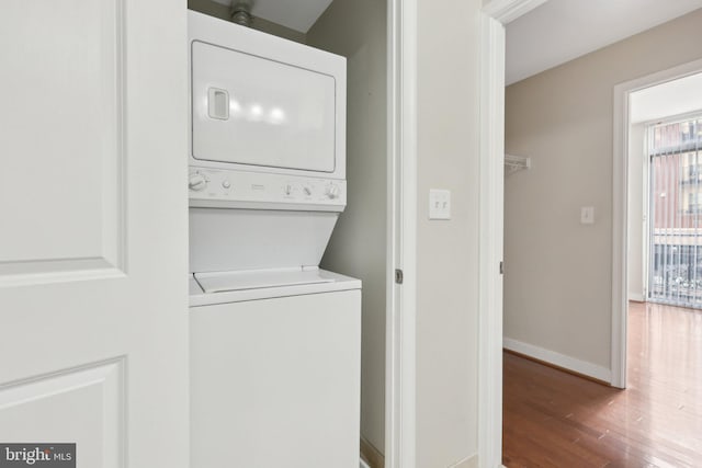 washroom with estacked washer and dryer, wood finished floors, and baseboards