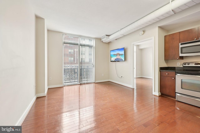 kitchen with stainless steel electric range, white microwave, dark countertops, light wood-type flooring, and baseboards