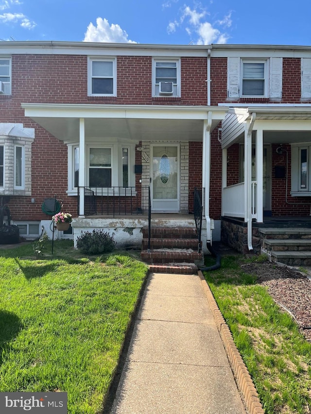 multi unit property with covered porch, brick siding, a front lawn, and cooling unit