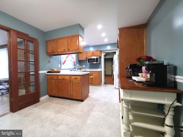 kitchen featuring stainless steel microwave, brown cabinets, a peninsula, french doors, and baseboards