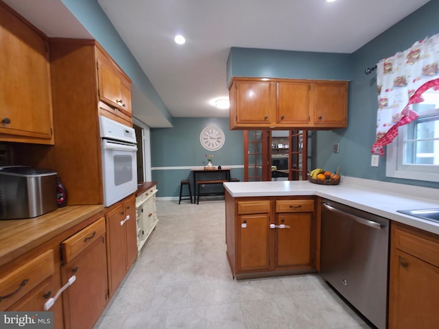 kitchen featuring white oven, dishwasher, brown cabinetry, light countertops, and a peninsula