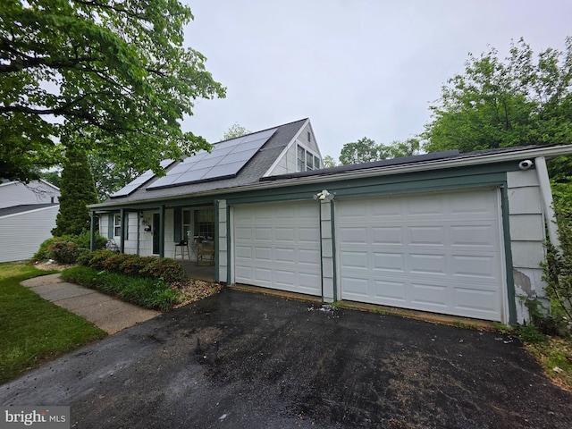 view of front facade featuring driveway, an attached garage, roof mounted solar panels, and covered porch