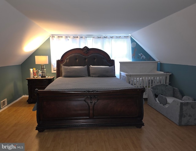 bedroom featuring wood finished floors, vaulted ceiling, multiple windows, and baseboards
