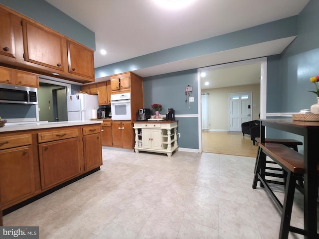 kitchen with white appliances, brown cabinets, light countertops, recessed lighting, and baseboards