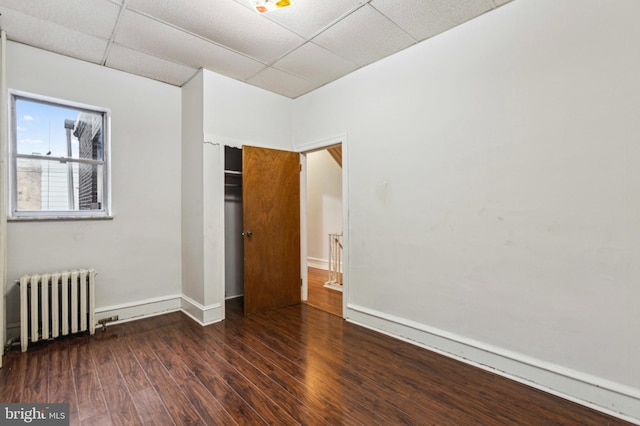 empty room featuring radiator, wood finished floors, baseboards, and a drop ceiling