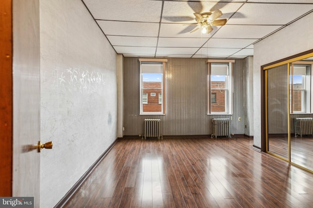 unfurnished bedroom with radiator heating unit, a paneled ceiling, wood-type flooring, a textured wall, and baseboards