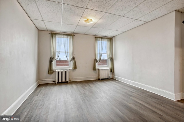 spare room featuring radiator heating unit, wood finished floors, a paneled ceiling, and baseboards